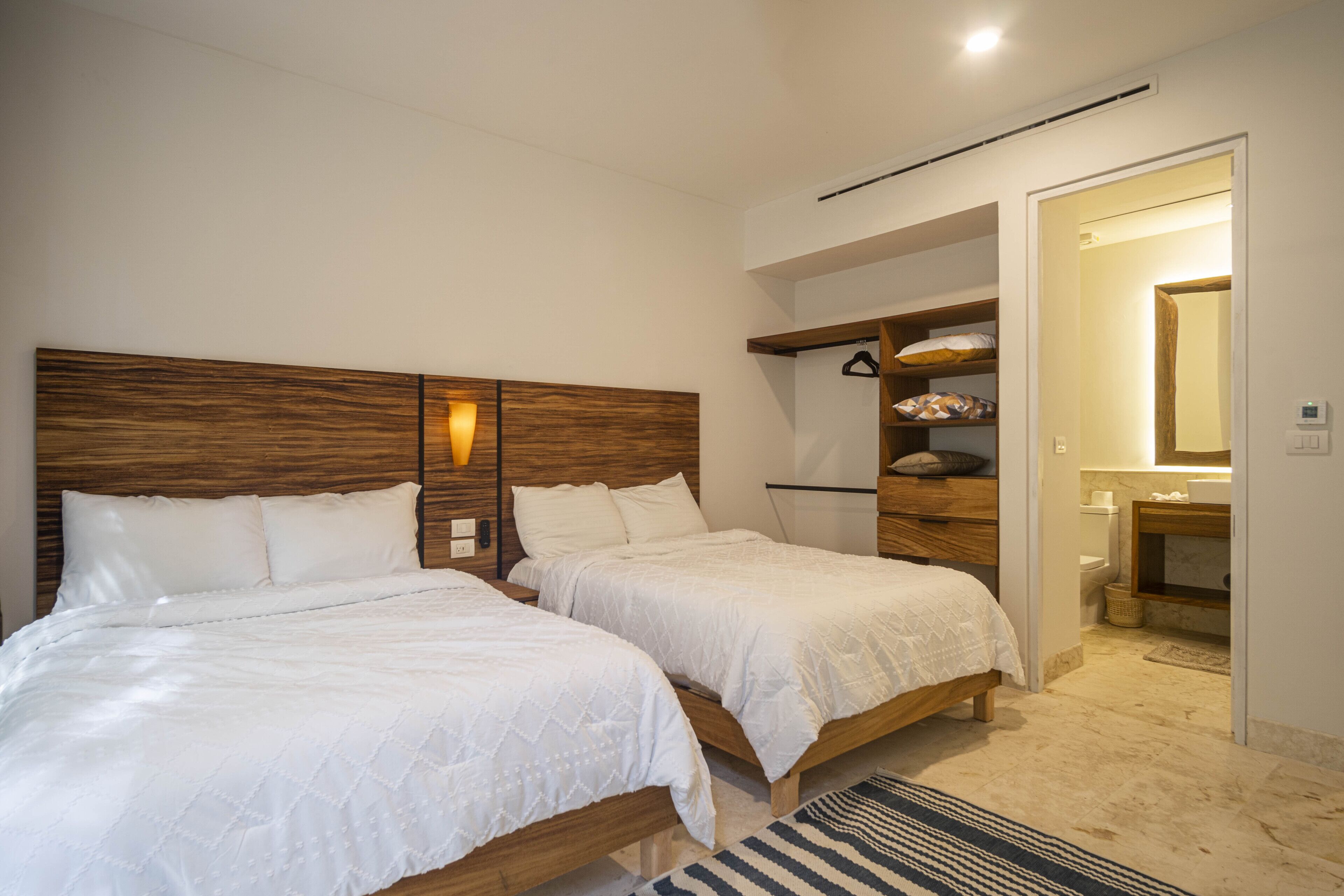 A bedroom with two beds, a wooden headboard, a bedside table, and a bathroom visible through an open door.