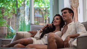 A couple sitting on a couch in a room with large windows and a view of greenery outside. - Vita Tulum (Tulum)