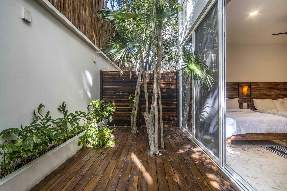 Un dormitorio moderno con un ventanal grande, suelo de madera y cama con ropa de cama blanca.