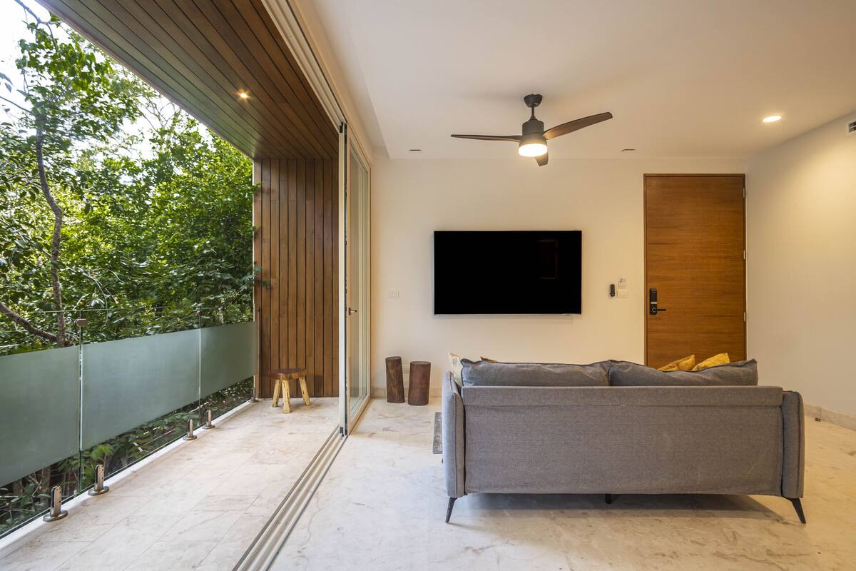Una sala de estar moderna con un sofá gris, un televisor montado y un ventilador de techo.