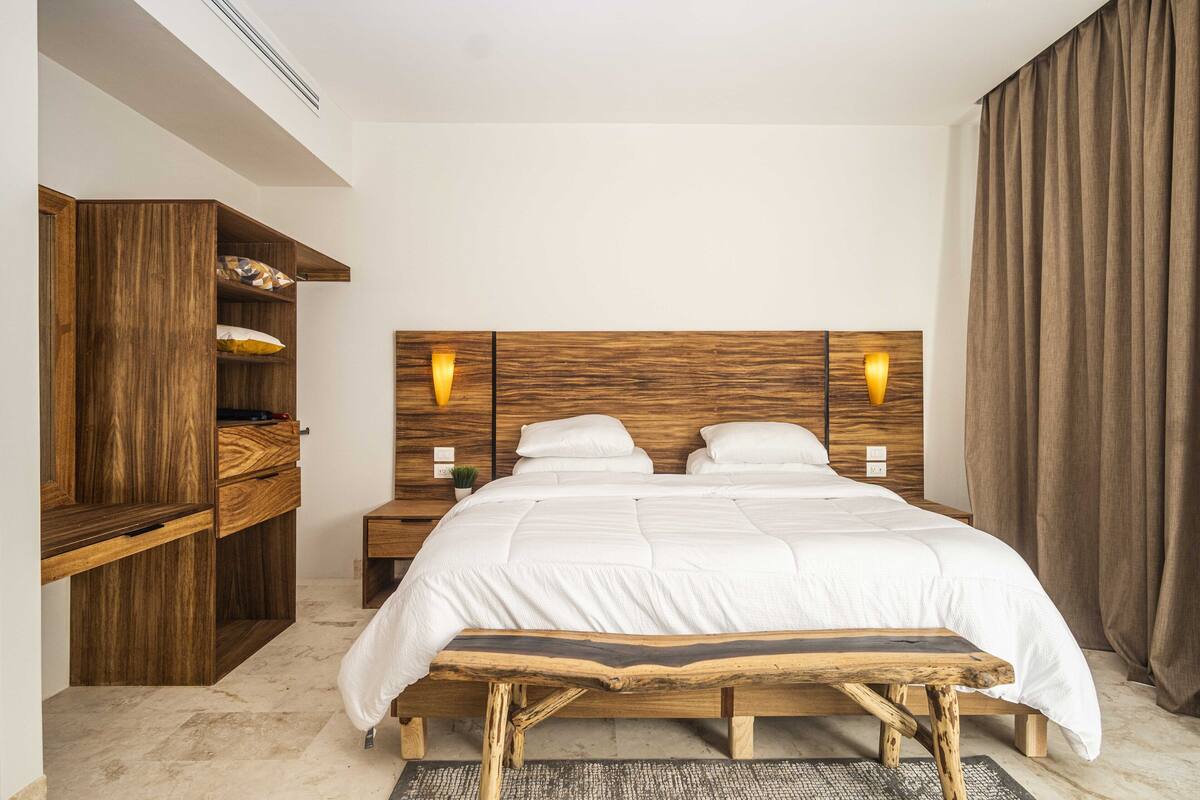 Un dormitorio con estructura de cama de madera, dos mesitas de noche, un armario empotrado y un ventanal con cortinas.