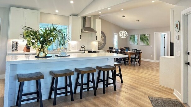A spacious kitchen with a large island, bar stools, and a dining area with a wooden table and chairs. - SunCoast Luxury Estates-New, Spacious,  Large Heated Pool, 10 min to the Beach  (Venice)
