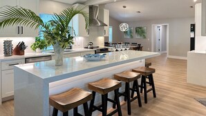A modern kitchen with a large island, bar stools, and a dining area with chairs and a table. - SunCoast Luxury Estates-New, Spacious,  Large Heated Pool, 10 min to the Beach  (Venice)