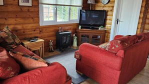 A cozy cabin-style room with a red sofa, a television, and a small cabinet. - Log Cabin - Free Parking, Garden & pet Friendly (Blaenau Ffestiniog)