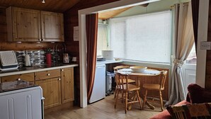 A compact kitchen with wooden cabinets, a small refrigerator, a coffee machine, and a dining table with chairs. - Log Cabin - Free Parking, Garden & pet Friendly (Blaenau Ffestiniog)