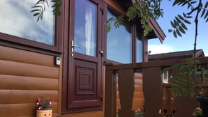 A wooden cabin with a large front door, a small porch with a flower pot, and a wooden fence. - Log Cabin - Free Parking, Garden & pet Friendly (Blaenau Ffestiniog)