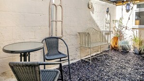 A courtyard with a stone wall, a metal bench, and wicker furniture.