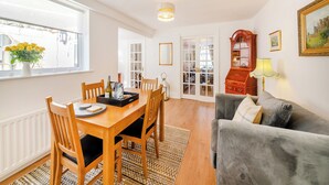 A dining area with a wooden table and chairs, a window with a vase of flowers, and a view of the street.