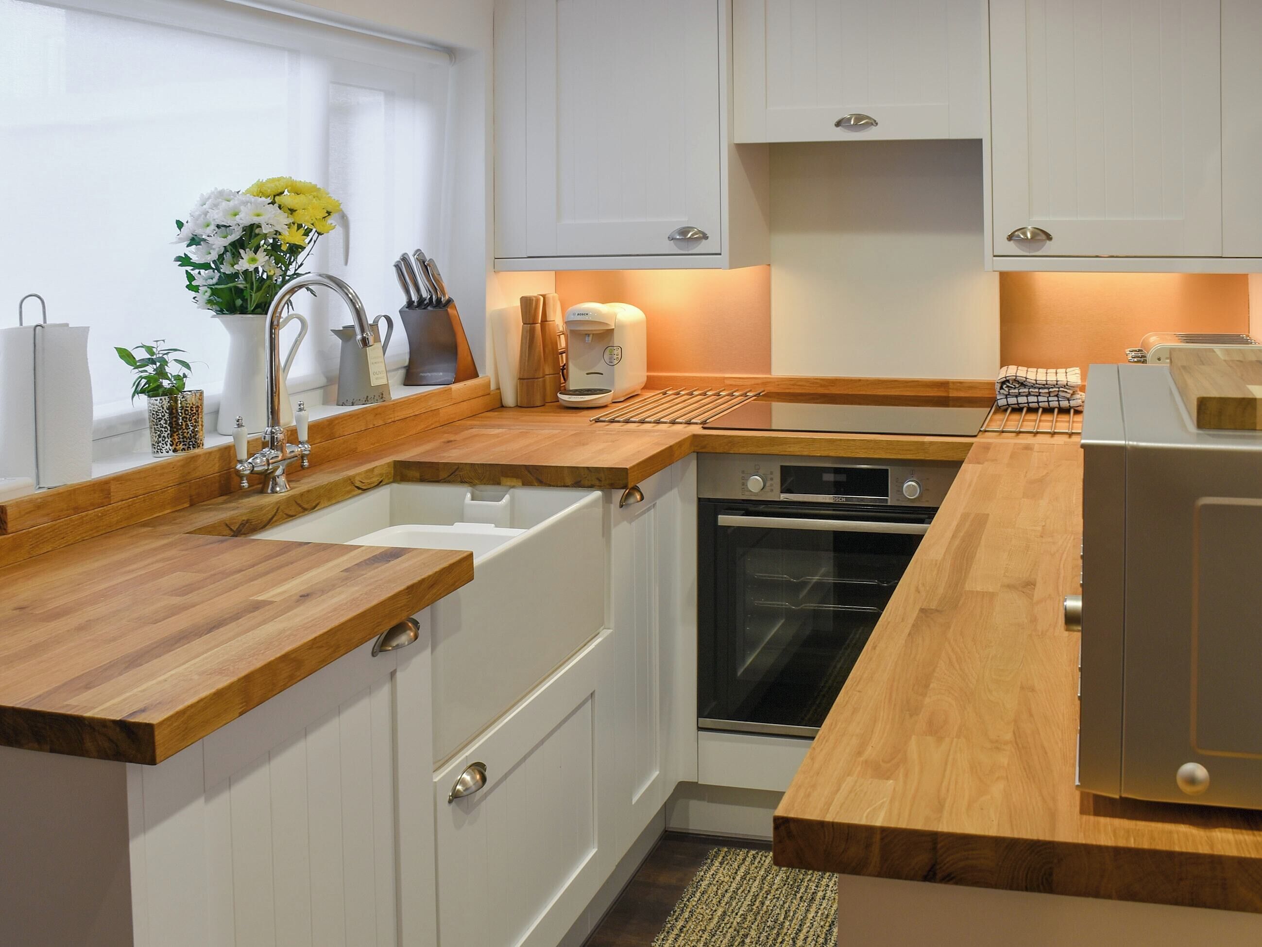 Een moderne keuken met witte kasten, een houten aanrecht, een ingebouwde oven en een koffiezetapparaat.