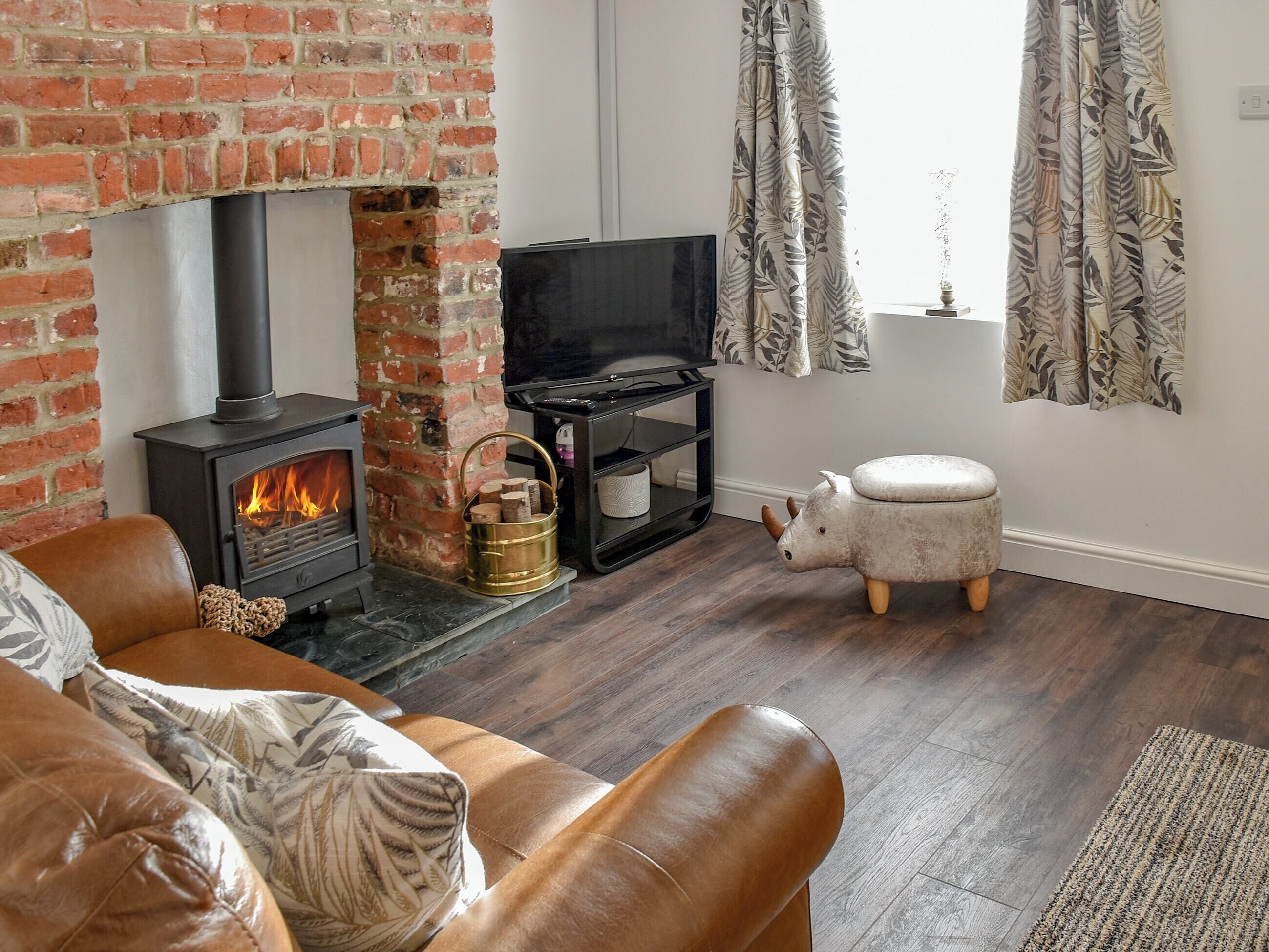 A cozy living room with a brick fireplace, a television, and a decorative sheep stool.