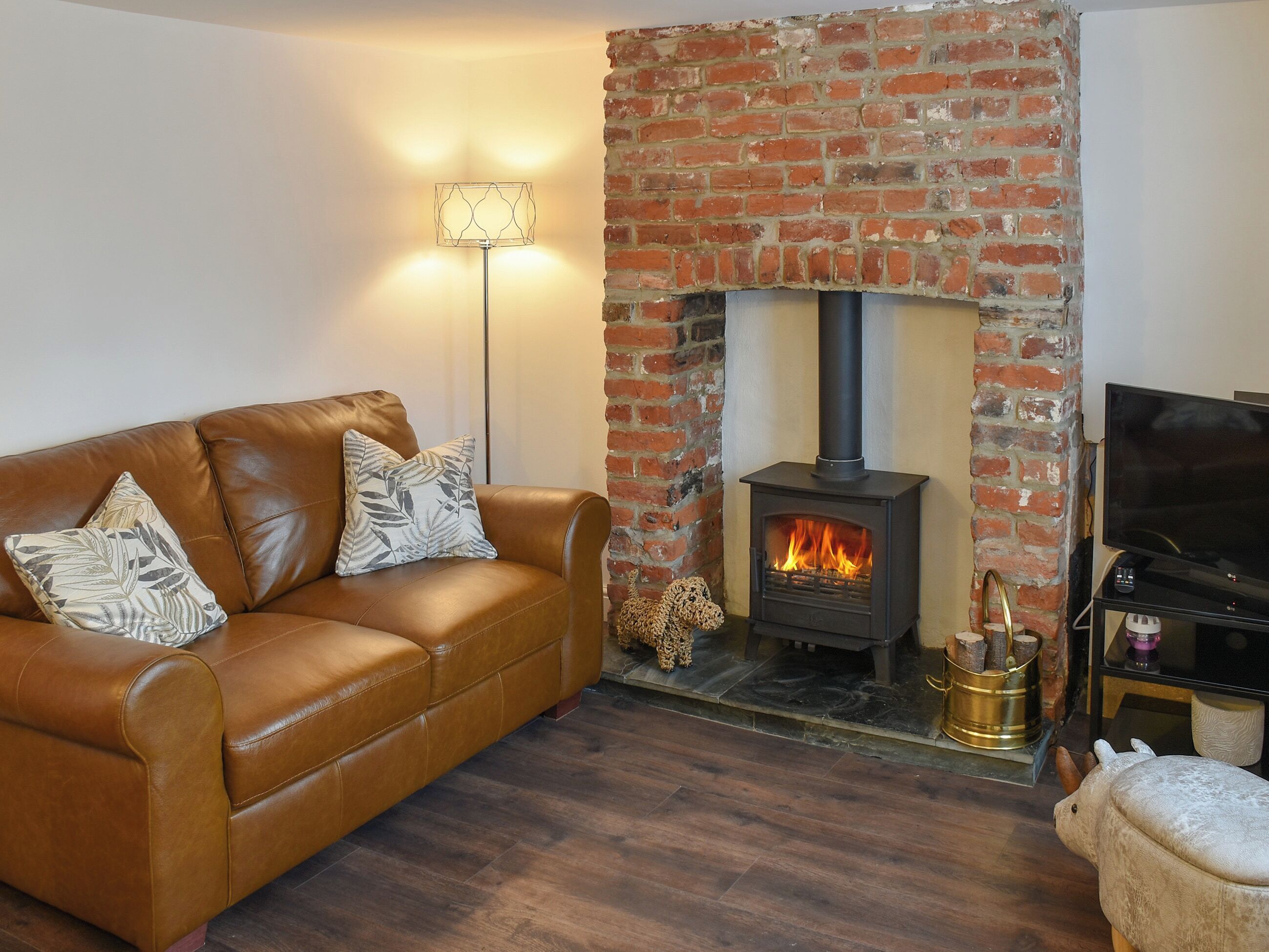 A cozy living room with a brick fireplace, leather sofa, and a television.