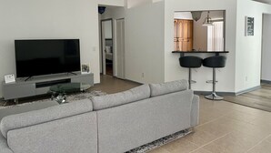 A living room with a flat-screen TV, grey sofa, ceiling fan, and a small glass table. - 3 Bedroom home with large pool. Great location. (Port St. Lucie)