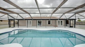 A swimming pool with a covered patio area, a building with multiple doors and windows, and a cloudy sky. - 3 Bedroom home with large pool. Great location. (Port St. Lucie)