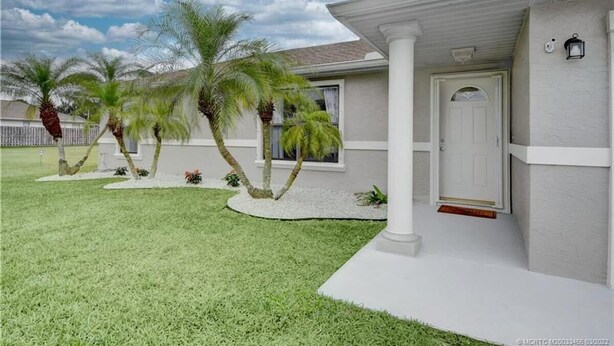 A residential house with a white exterior, a covered porch, and a well-maintained lawn with palm trees. - 3 Bedroom home with large pool. Great location. (Port St. Lucie)