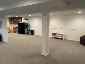 A spacious living area with a kitchen in the background, a white bench, and a white column.