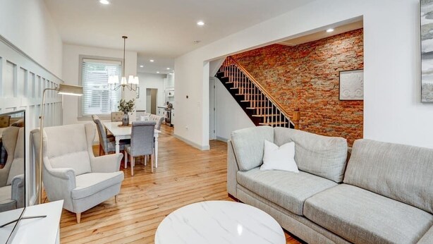 A modern living room with a grey sofa, a round coffee table, and a staircase with a brick wall. - Luxury Manor on Mulberry in the heart of Downtown Lanc (Lancaster)