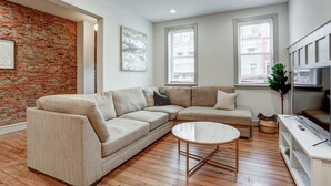 A living room with a sectional sofa, a round coffee table, and a brick accent wall. - Luxury Manor on Mulberry in the heart of Downtown Lanc (Lancaster)