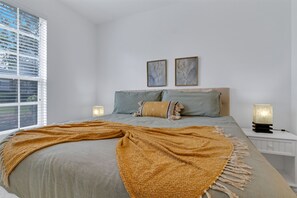 Quarto com cama, duas almofadas, um cobertor, mesa de cabeceira com abajur e duas quadros na parede.