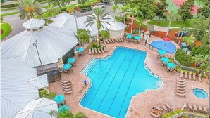A large outdoor swimming pool with lounge chairs and umbrellas, surrounded by palm trees and a tennis court. - Newly Renovated First Floor 2Bed & 2 Bath, Near Disney (Kissimmee)