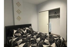 Relax in a stylish bedroom with a geometric-patterned bedspread, a wardrobe with a mirrored door, and a convenient shelf for storage.
