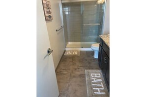 Bathroom features a glass-enclosed shower, toilet, and dark cabinet.