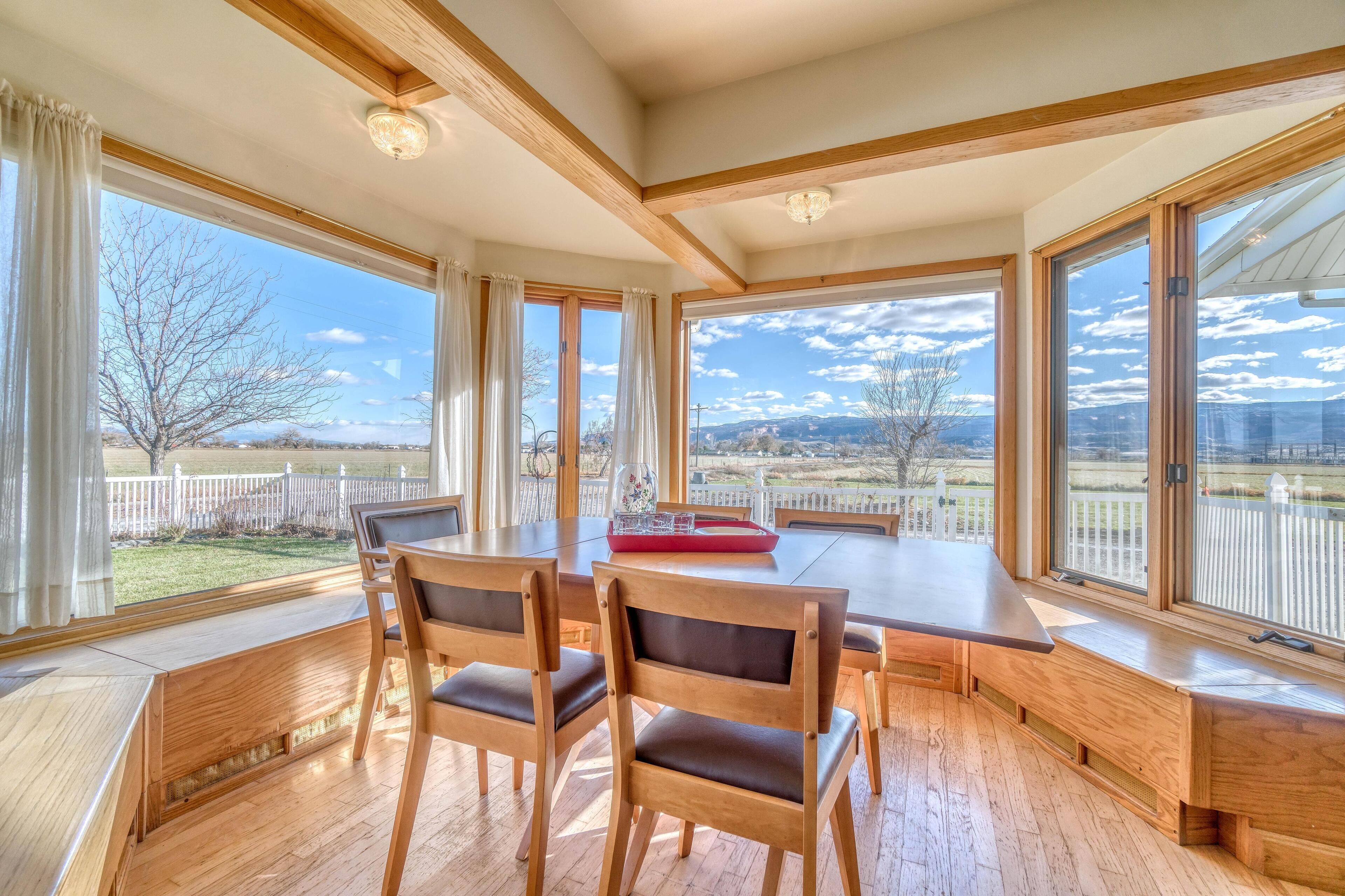 Ein Essbereich mit Holztisch und Stühlen, große Fenster mit Blick auf einen umzäunten Garten und Berge.