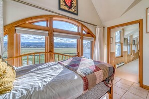 A bedroom with a large window, a bed with a quilt, and a view of the countryside. - Shady Acres: Two Living Spaces & Curated Library (Fruita)
