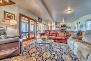A spacious living room with a large window, a leather sofa, a glass coffee table, and a patterned rug. - Shady Acres: Two Living Spaces & Curated Library (Fruita)