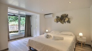 Ein Schlafzimmer mit einem großen Bett, zwei Nachttischen mit Lampen, einer Wand-Klimaanlage und einer Glastür, die zu einem Außenbereich führt.