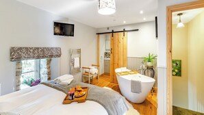 A modern bedroom with a large bed, a wooden bathtub, a TV, and a breakfast tray.
