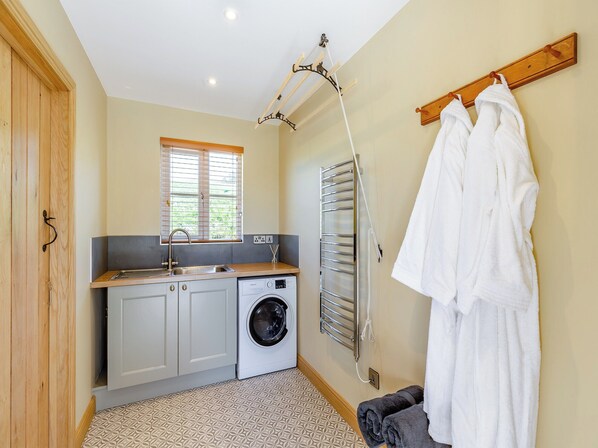 A compact laundry room with a washing machine, drying rack, and a window with blinds. - 1 bedroom accommodation in Llandrinod Wells (Llandrinod Wells)