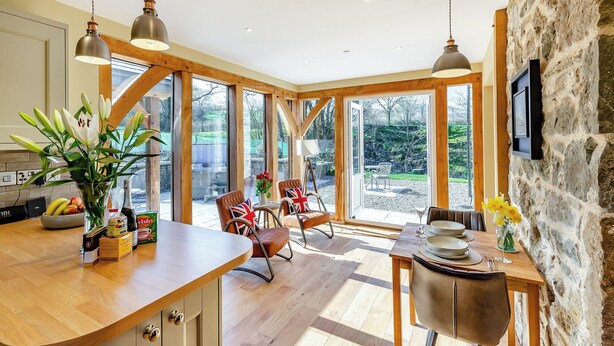 A spacious kitchen with wooden beams, large windows, and a stone wall.