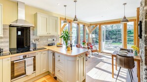 A modern kitchen with a central island, wooden beams, and large windows offering a view of the outdoors.