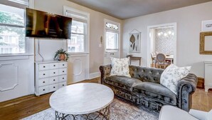 A living room with a sofa, a round coffee table, a television, and a chandelier.