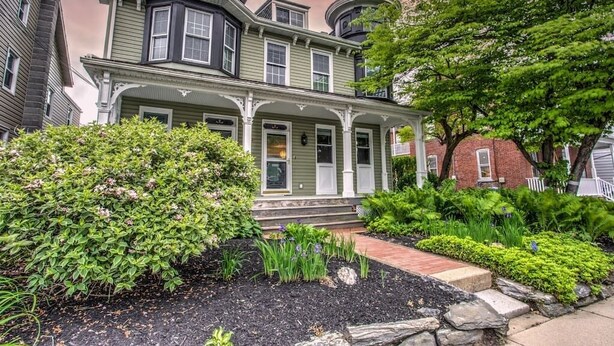 A Victorian-style house with a wrap-around porch, brick foundation, and a turret.