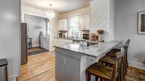 A modern kitchen with white cabinetry, a central island with bar stools, a chandelier, and a view of the adjacent dining area.