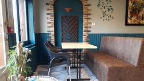 A corner seating area with a sofa, a table, and chairs. There is a decorative wall with a brick pattern and a plant on the floor. - Le Salençon (Foissiat)