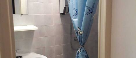 A small bathroom with a white sink, a toilet, and a shower curtain with a sea-themed pattern.