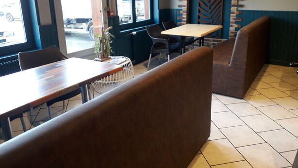A restaurant interior with booth seating, a brick accent wall, and a view of the street through large windows. - Le Salençon (Foissiat)