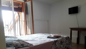 A bedroom with a bed, a small table, a TV, and a window with curtains. - Le Salençon (Foissiat)