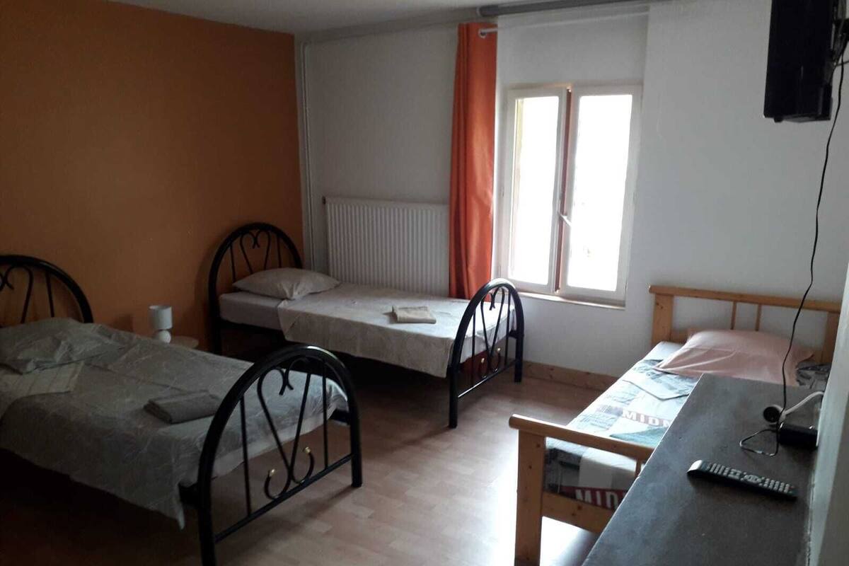 A small, simple room with two single beds, a wooden desk, and a window with curtains.