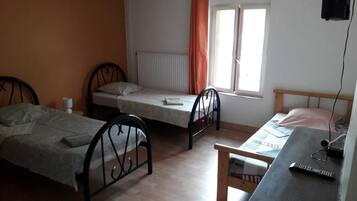 A small, simple room with two single beds, a wooden desk, and a window with curtains.