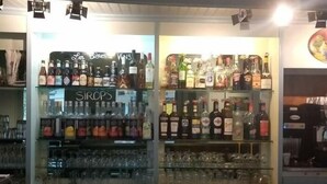 A bar area with shelves stocked with various liquor bottles and glasses. - Le Salençon (Foissiat)