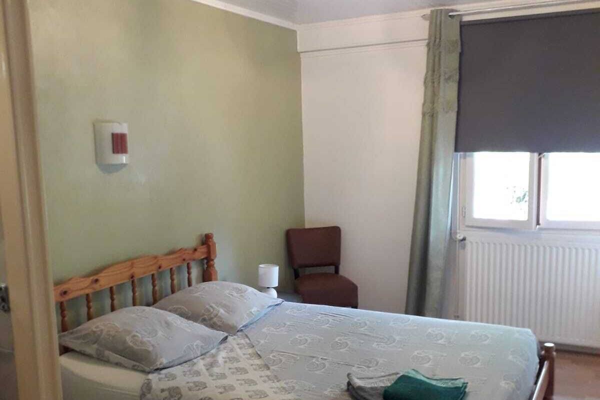 A bedroom with a wooden bed, a chair, a radiator, and a window with curtains.