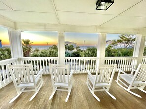 A covered outdoor seating area with white chairs and a view of the sunset over the ocean.