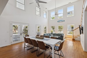 A spacious dining area with a white table and brown chairs, a gray sofa, and a ceiling fan.
