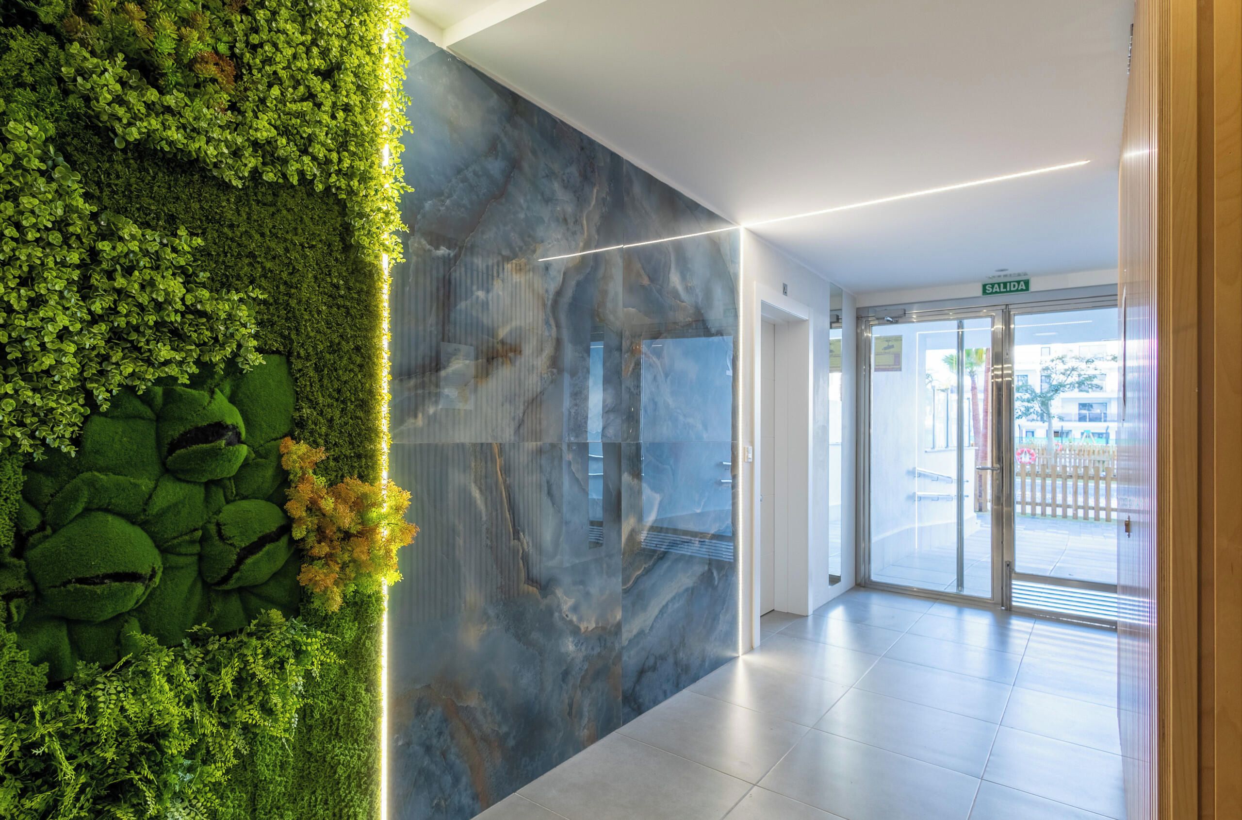 Een moderne lobby met een groene verticale tuin, een marmeren wand en een glazen deur die naar buiten leidt.