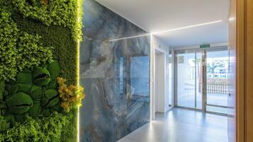 Een moderne lobby met een groene verticale tuin, een marmeren wand en een glazen deur die naar buiten leidt.