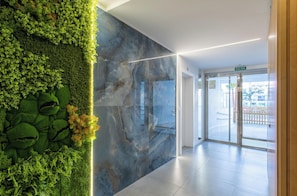 Un vestíbulo moderno con un jardín vertical verde, una pared de mármol y una puerta de vidrio que da al exterior.