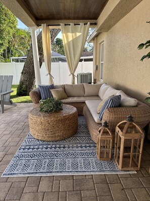 Ein überdachter Patio-Bereich mit einer Eckcouch, Korpus-Ottomanen, einem gemusterten Teppich und hölzernen Laternen.